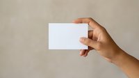 Close-up of a hand holding a blank white card against a neutral beige background, suitable for business card mockups and branding presentations.