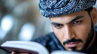 Young Middle Eastern man in traditional headscarf reading religious book with focused expression. Spiritual education and religious study concept captured in natural lighting.