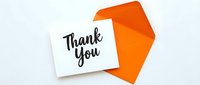 Thank you card with black handwritten lettering leaning against a bright orange envelope on a white background.