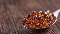 Omega-3 fish oil capsules in silver spoon on wooden background, nutritional supplement and healthy lifestyle concept, macro photography with soft focus.