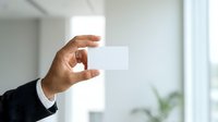 Businessman holding blank white business card in modern office environment with natural light and blurred background, suitable for corporate branding and professional networking concepts.