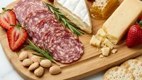 Gourmet charcuterie board with sliced salami, aged cheese, fresh strawberries, nuts and crackers on wooden cutting board for entertaining and appetizers.
