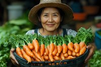 Senior Asian woman in straw hat holding fresh harvested organic carrots at farmers market, showcasing sustainable agriculture and healthy food.