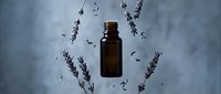 Amber glass essential oil bottle surrounded by fresh lavender sprigs on light background for aromatherapy and natural wellness products.