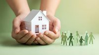 Hands protecting white paper house model with green family figures, symbolizing home insurance, real estate protection, and family security concept.