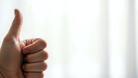 Hand showing thumbs up gesture against soft white background expressing approval, success and positive feedback for business presentations.