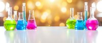 Laboratory glassware with colorful chemical solutions on white surface against golden bokeh background for science education and research.