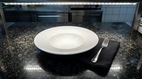 Empty white plate with fork on black napkin atop speckled granite countertop in modern kitchen, suitable for food styling, restaurant menus, culinary blogs, and dining concepts.