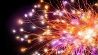 Vibrant abstract light trails burst outward in orange, purple and white against black background, creating dynamic energy pattern for creative backgrounds.