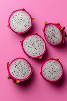Fresh dragon fruit slices arranged on pink background showing white flesh with black seeds, creating minimal food composition for healthy eating concept.