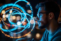 Young caucasian man with glasses in profile view surrounded by glowing blue and orange light trails and bokeh effects creating magical atmosphere for technology concept.