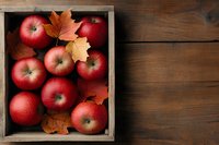 Fresh red apples in rustic wooden box with autumn maple leaves on dark wooden background, top view composition for seasonal food and harvest concept.