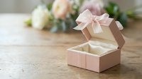 Open pink gift box with satin ribbon bow on wooden table with soft floral background for special occasions and celebrations.