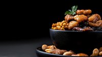 Mixed roasted nuts and seeds in black ceramic bowl on dark background with copy space, selective focus on glazed cashews and almonds with honey coating.