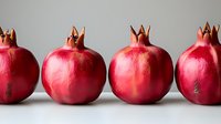 Fresh ripe pomegranates arranged in row on light background, bright red fruits with distinctive crowns showing natural organic produce.