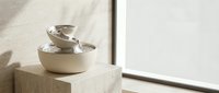 Minimalist ceramic pet water fountain on a stone pedestal near a bright window, soft natural light, modern interior design aesthetic.
