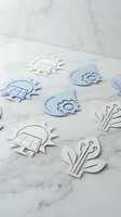 Paper cut eco technology icons in blue and white tones on marble surface, featuring solar panels, water drops, gears, and digital plants.