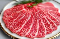Fresh marbled beef slices arranged in fan pattern on white plate with gold rim, showing distinctive red and white fat streaking characteristic of premium meat.