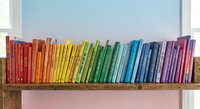Colorful books arranged by rainbow spectrum on wooden shelf creating organized library display for education and reading concepts.