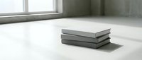 Stack of three hardcover books in neutral gray tones on white floor near window with natural light for modern minimalist interior design concepts.
