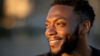 Young African American man with bright genuine smile looking away during golden hour sunset, natural lighting creates warm glow on skin, casual portrait outdoors.