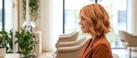 Professional middle-aged Caucasian businesswoman with wavy auburn hair in modern office interior with plants and natural lighting for corporate content.