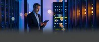 Professional businessman using smartphone in modern data center with server racks and glowing lights for technology and business communications.