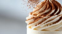 Swirled cream dessert topping dusted with cocoa powder on light background, macro close up view of whipped dairy texture for pastry and baking designs.