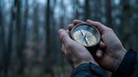 Hands holding vintage compass in dark forest showing direction and navigation concept for outdoor adventure and exploration activities.