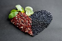 Heart shape made from red quinoa and black caviar garnished with fresh baby spinach leaves on dark background, healthy superfood concept.