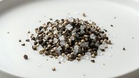 Mixed peppercorns pile on white plate featuring black white green pink varieties for seasoning cooking spice blend culinary ingredient kitchen preparation.