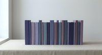Row of purple and blue books arranged on white shelf creating minimalist home decor display for interior design and organization concepts.