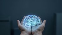 Glowing holographic brain floating above open hands in dark room representing artificial intelligence, neuroscience and mental health concepts.