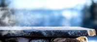 Rustic stone surface with rising steam against blurred winter background creates atmospheric mood for food photography and product presentation.