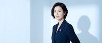 Professional Asian businesswoman in navy suit standing confidently against modern blue background for corporate presentations and marketing materials.