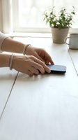 Woman hands using smartphone on white wooden table with coffee cup and plant in bright natural light for communication and lifestyle.