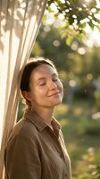 Young woman with closed eyes enjoying peaceful moment by window curtain in warm sunlight with natural bokeh background for wellness and mindfulness concepts.