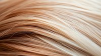 Close-up of flowing blonde hair strands with natural highlights and lowlights showing smooth texture and shine for beauty and haircare concepts.