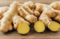 Fresh ginger root with sliced pieces showing bright yellow flesh on wooden background, natural organic spice and herbal medicine ingredient.