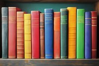 Colorful hardcover books arranged in row on wooden shelf, spines showing vibrant mix of red, blue, green, and yellow bindings. Classic library collection display.