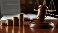 Wooden gavel with stacked gold coins and scales of justice on desk representing legal fees, financial law, court costs, and judicial system expenses.