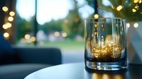 Whiskey glass with golden liquid on dark table against blurred bokeh lights background creates cozy evening atmosphere. Suitable for beverage advertising.