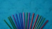 Colorful reusable metal drinking straws arranged in fan pattern on textured turquoise background for eco-friendly lifestyle and zero waste concept.