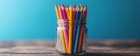 Colorful wooden pencils standing upright in clear glass jar against turquoise blue background, creative art supplies on rustic wooden table surface, minimal composition.