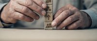 Senior businessman hands stacking wooden blocks with business icons representing strategic planning and corporate growth solutions.