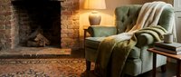 Cozy living room interior with green armchair, warm throw blanket, brick fireplace and soft lighting creating comfortable home atmosphere for relaxation.