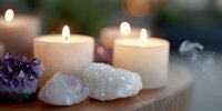 Glowing candles alongside amethyst and quartz crystal clusters on wooden surface create serene spiritual atmosphere for meditation and mindfulness practices.