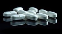 White oval pharmaceutical tablets scattered on reflective black surface with dramatic lighting and shadows, suitable for medical and healthcare publications.