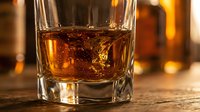 Premium whiskey in crystal tumbler glass with amber liquid and warm golden lighting for luxury beverage photography and sophisticated drinking concepts.