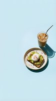 Overhead flat lay of avocado toast with poached egg and iced coffee on light blue background. Perfect for food blogs, cafes, brunch menus, and wellness content.